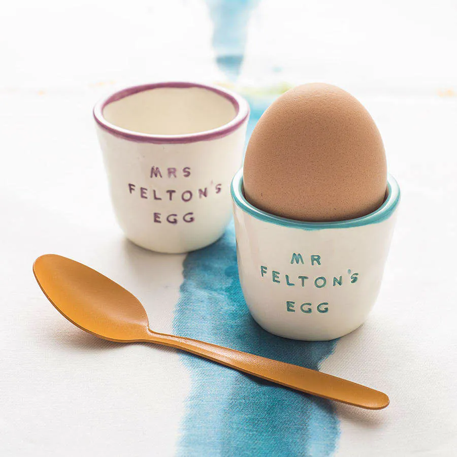 Not On The High Street Handmade in a small studio in Cornwall, these white ceramic egg cups have a colourful rim and hand-stamped name in matching glaze, making the perfect gift.