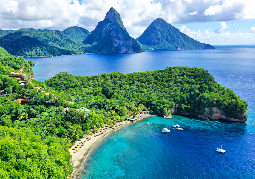 Aerial view of Anse Chastanet in St Lucia, with a curving beach, turquoise bay and the twin Pitons beyond
