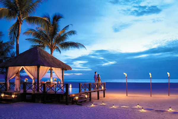 Couple on a beachside deck at dusk beside a candlelit gazebo and lanterns on the sand in Borneo