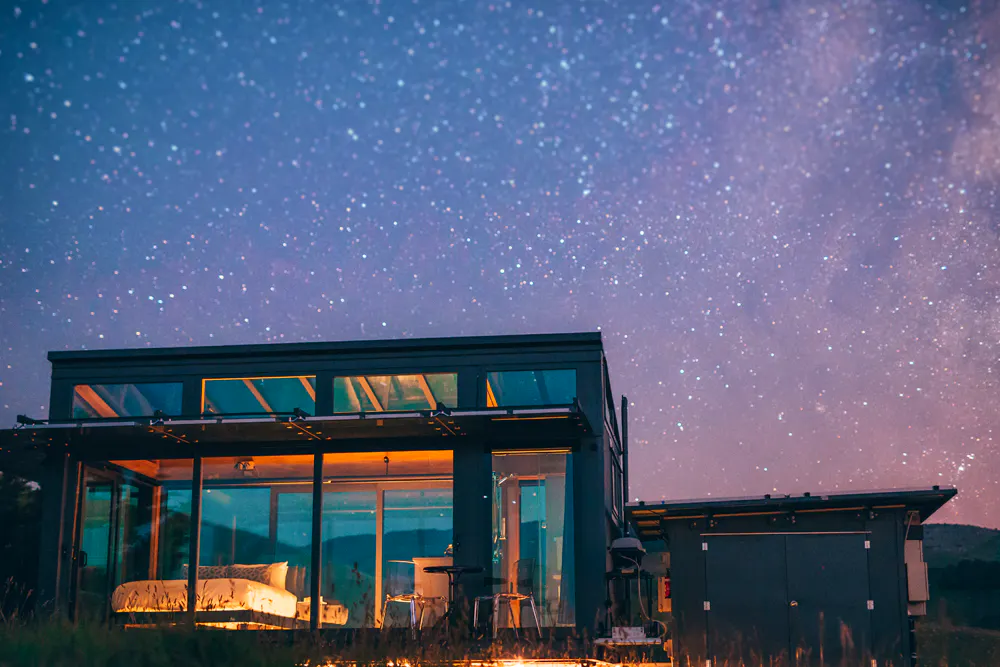 Glass-walled PurePod lit up at night beneath a starry sky in New Zealand