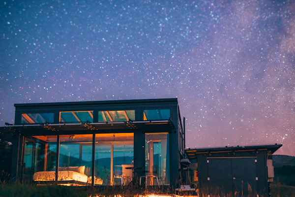 Glass-walled PurePod lit up at night beneath a starry sky in New Zealand