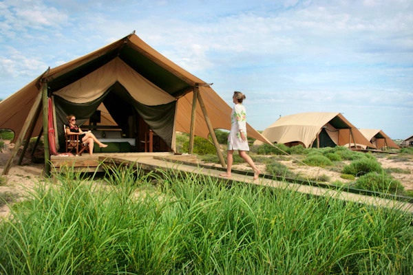 Safari-style tents among dunes and grass at Sal Salis on Ningaloo Reef, with two women outside