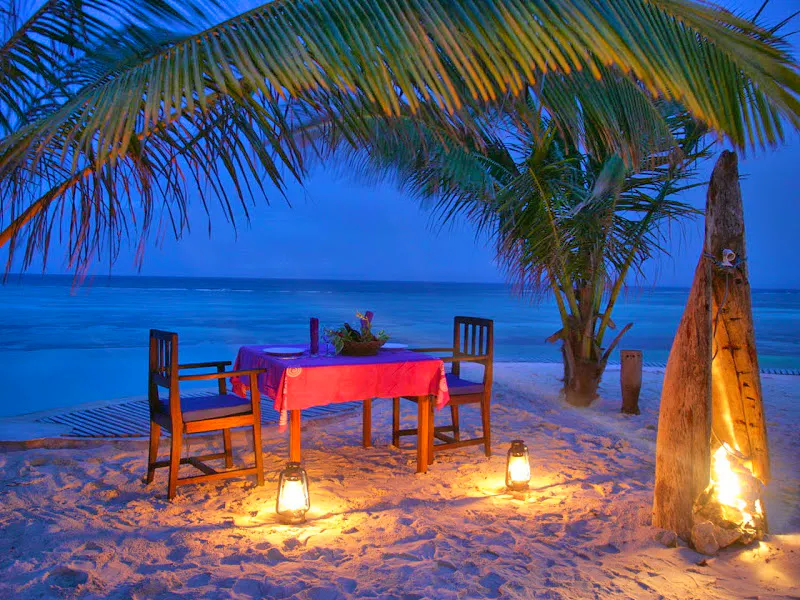Lantern-lit table and chairs on a Zanzibar beach under palm trees at dusk